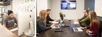 Engineer sits at an iMac while team members meet in a conference room