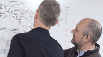Photo of IT pros looking at a whiteboard with systems architecture blueprints