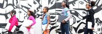 Image of black girls walking in front of graffiti with laptops