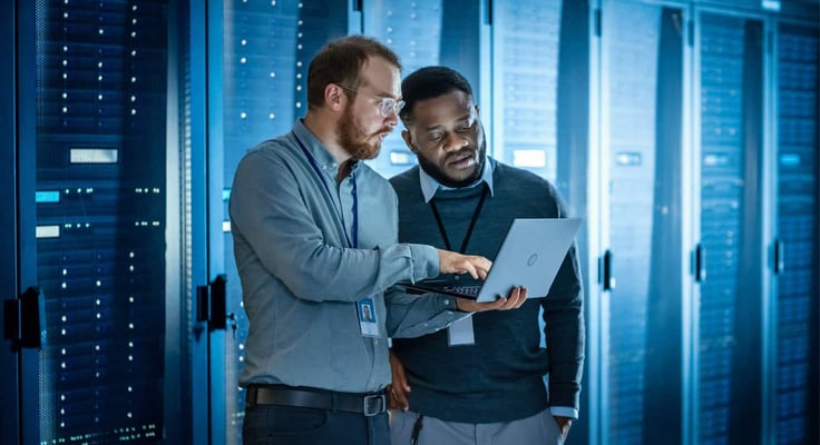 Two men in front of a laptop in a server room Two men in front of a laptop in a server room