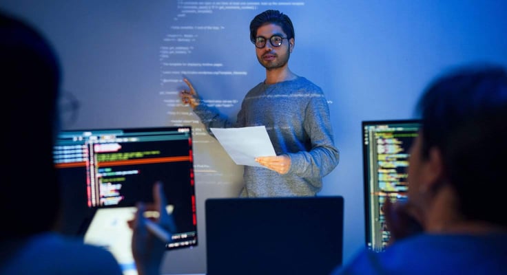 Asian developer leads present code review session, pointing at code projected on the wall with colleagues  teamwork and knowledge sharing in software development