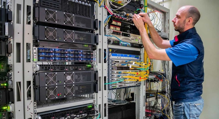 A man commutes wires in a server room. A technician works with server equipment in a data center.