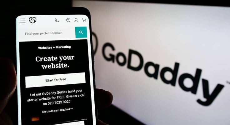 Person holding smartphone with website of American web hosting company GoDaddy Inc. on screen in front of logo