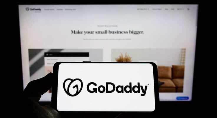 Person holding smartphone with logo of US web hosting company GoDaddy Inc. on screen in front of website. Focus on phone display