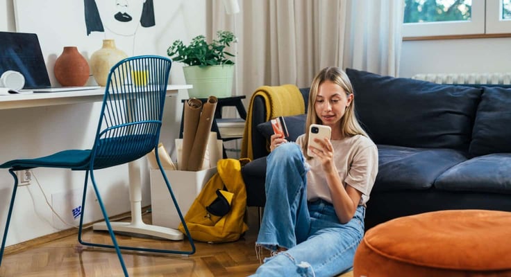 European teenager female shopping online using her mobile phone while sitting in her room
