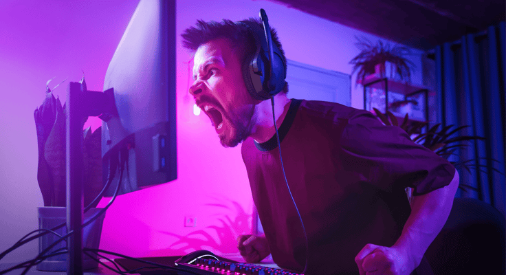 Young man plays computer games at home. The player is upset about the defeat. The streamer is angry during the broadcast. Neon studio setting. Guy surfing the Internet with headphones