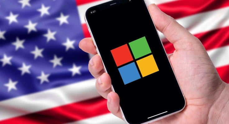 Microsoft logo on the screen of the smartphone standing in front of the blurred American flag