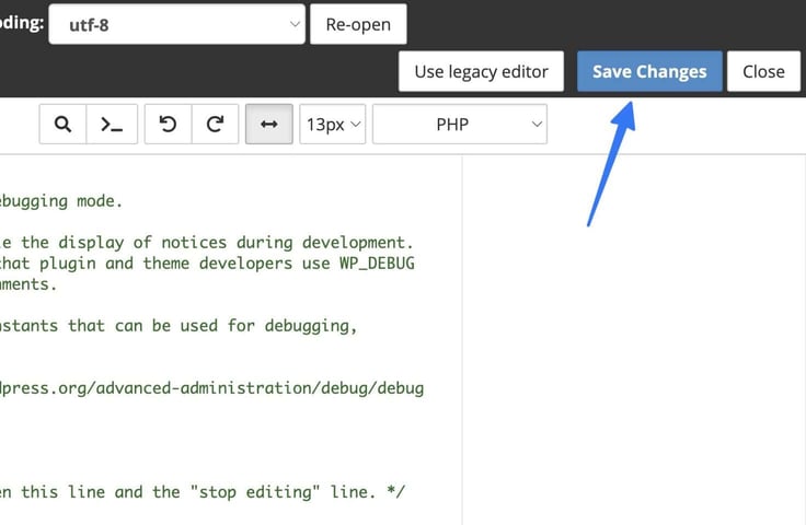 A code editor toolbar for a PHP file shows encoding set to utf-8 with a Re-open button, plus Use Legacy Editor, Save Changes, and Close buttons at the top, where a blue arrow points directly to the Save Changes button needed to commit wp-config.php edits, with visible debugging-related comment text in the code pane below. A code editor toolbar for a PHP file shows encoding set to utf-8 with a Re-open button, plus Use Legacy Editor, Save Changes, and Close buttons at the top, where a blue arrow points directly to the Save Changes button needed to commit wp-config.php edits, with visible debugging-related comment text in the code pane below.