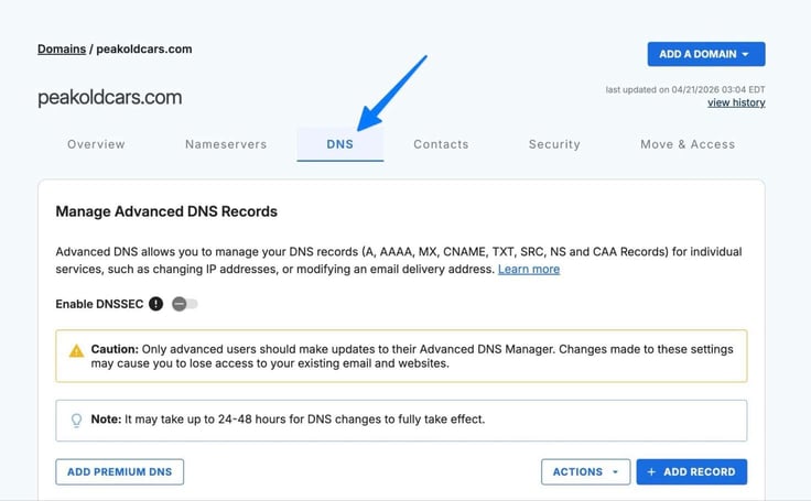 The domain management page for peakoldcars.com displays tabs for Overview, Nameservers, a selected DNS tab (indicated by a blue arrow), Contacts, Security, and Move & Access, above a "Manage Advanced DNS Records" section featuring a DNSSEC toggle, a caution notice about advanced users only, a note about 24-48 hour DNS propagation, and "Add Premium DNS" and "+ Add Record" buttons in the upper right, alongside an "Add A Domain" dropdown button. The domain management page for peakoldcars.com displays tabs for Overview, Nameservers, a selected DNS tab (indicated by a blue arrow), Contacts, Security, and Move & Access, above a "Manage Advanced DNS Records" section featuring a DNSSEC toggle, a caution notice about advanced users only, a note about 24-48 hour DNS propagation, and "Add Premium DNS" and "+ Add Record" buttons in the upper right, alongside an "Add A Domain" dropdown button.