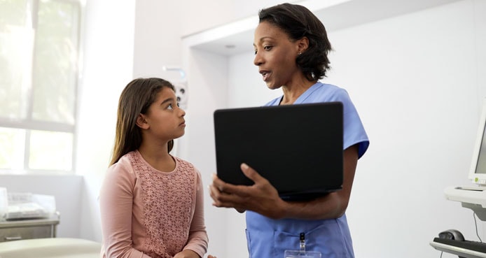 Photo of a doctor holding a computer providing care to a child Photo of a doctor holding a computer providing care to a child