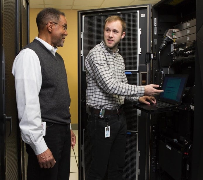Photo of two men talking near a mainframe Photo of two men talking near a mainframe